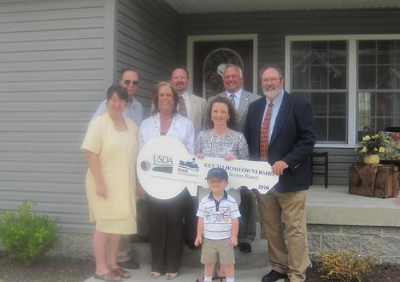 Rural Development employees with West Virginia homeowners in front of their new home.  Row 1:  Connor Sexton.  Row 2 (l to r):  Penny Thaxton (Housing Specialist); Shelly Hickman (Area Specialist); Homeowner Jamalyn Sexton; and Craig Burns (Area Director).  Row 3 (l to r):  Jeff Hunt (Area Specialist); David Cain (Acting Housing Program Director); and Bobby Lewis (State Director).