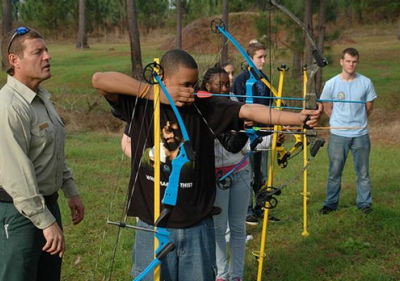 Natural Resource Manager Carl Petrick of the National Forests in Florida looks on as a high school student sets his sights on the archery range. Nearly 500 students from area schools attended the recent More Kids in the Woods event. (Photo Credit: Susan Blake, Public Affairs Specialist, National Forests of Florida)