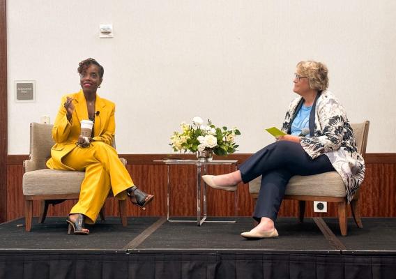 Two women sitting on a conference stage engaging in discussion
